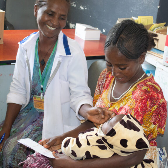 A health provider sits with a client and her newborn